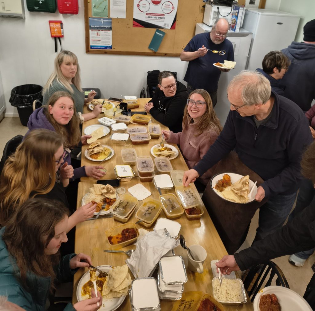 Photo of a group of Women Gliding visitors enjoying a curry & sitting around a table laden with takeaway boxes