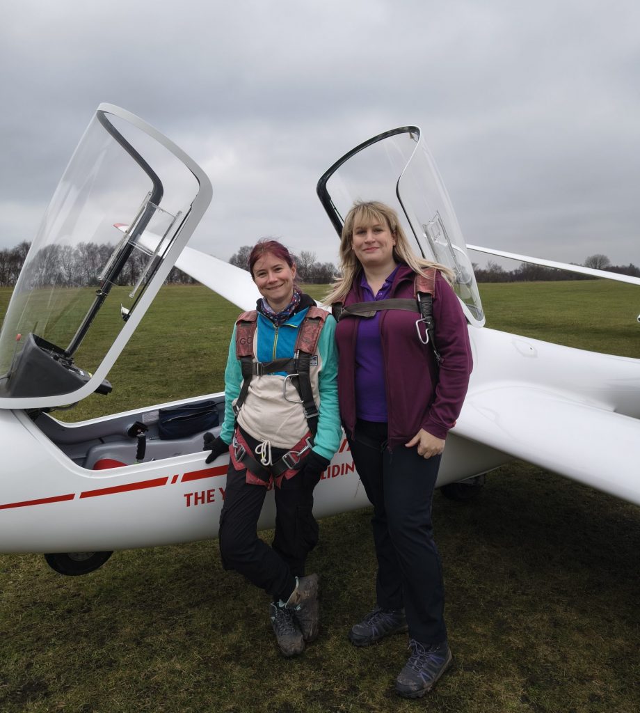 Photo of two female pilots standing in front of a two-seat glider.