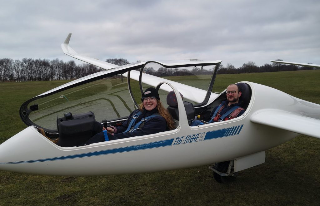 Photo of a female pilot sitting in the front seat of a two-seat glider with her instructor in the back, ready to fly.